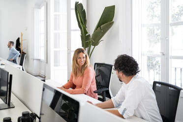 Smiling female entrepreneur looking at male coworker while sitting in office - MPPF01853