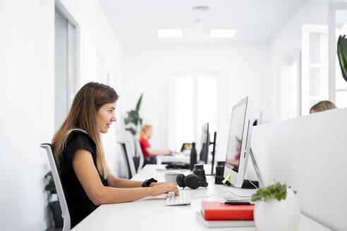 Geschäftsfrau arbeitet an einem Desktop-Computer, während sie in einem Coworking-Büro sitzt - MPPF01854