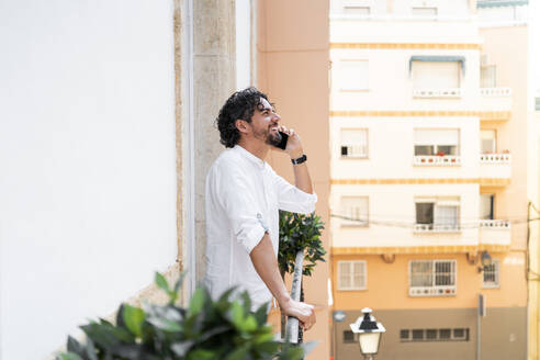 Male entrepreneur talking on smart phone while standing on office balcony - MPPF01855