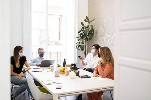 Männliche und weibliche Fachkräfte sitzen während der COVID-19 an einem Tisch im Coworking-Büro - MPPF01856