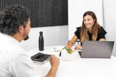 Smiling female entrepreneur discussing with businessman at coworking office - MPPF01863