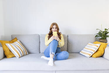 Woman surfing net through mobile phone while sitting on sofa in living room at home - WPEF04732