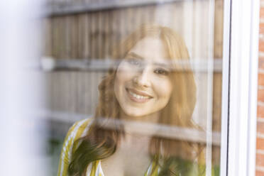 Beautiful smiling redhead woman seen through window - WPEF04739