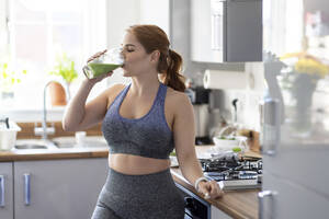 Rothaarige Frau trinkt gesunden Milchshake nach dem Training zu Hause - WPEF04797