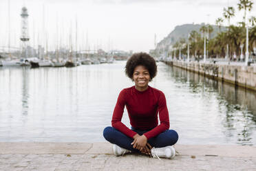 Junge Afro-Frau auf der Promenade in der Stadt sitzend - XLGF02030
