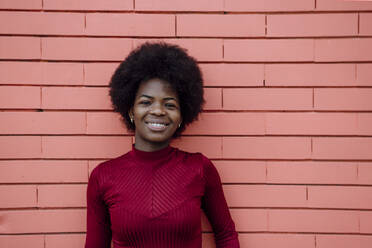 Smiling Afro woman standing in front of brick wall - XLGF02032