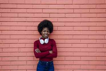 Afro woman with arms crossed standing by brick wall - XLGF02033