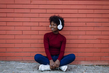 Young woman with headphones sitting cross-legged near brick wall - XLGF02039