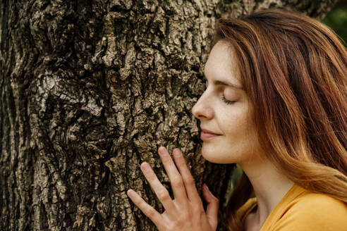 Smiling woman relaxing on tree trunk in garden - AFVF08788