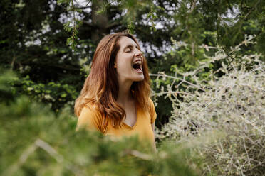 Redheaded woman screaming in garden with mouth open - AFVF08790