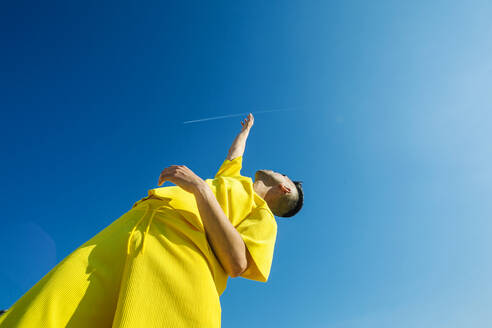 Young man looking up with hands raised in sky during sunny day - XLGF02049