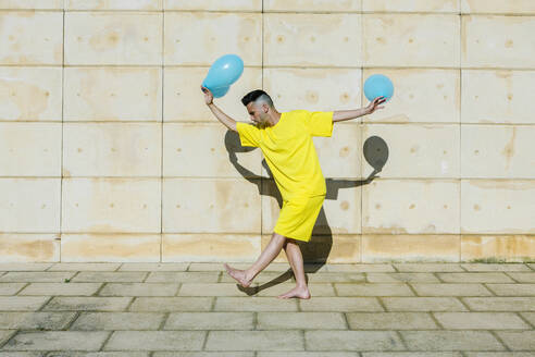 Junger Mann tanzt mit Luftballons in der Nähe der Wand während des sonnigen Tages - XLGF02050