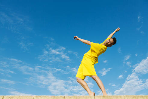 Junger Mann tanzt auf Stützmauer durch blauen Himmel - XLGF02054
