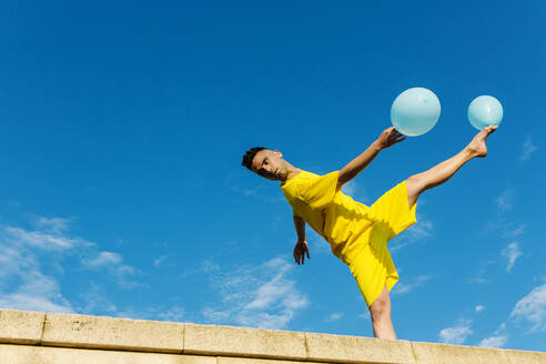 Junger Mann balanciert beim Tanzen mit Luftballons - XLGF02055