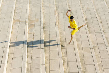 Junger Mann springt beim Tanzen auf einer Treppe an einem sonnigen Tag - XLGF02056