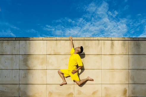Man hanging on wall with one hand during sunny day - XLGF02061
