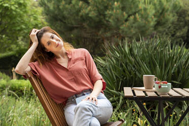 Schöne Frau mit Kopf in der Hand sitzt auf einem Stuhl im Garten - AFVF08795