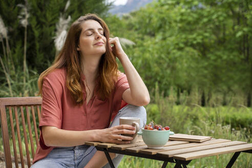 Beautiful woman sitting with eyes closed on chair in garden - AFVF08800