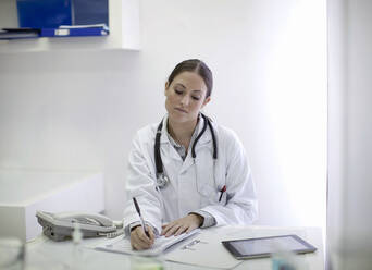 Weiblicher Arzt schreibt Bericht, während er am Tisch sitzt - AJOF01464