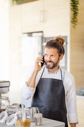 Männlicher Koch, der in einem Restaurant mit seinem Handy telefoniert - PGF00596