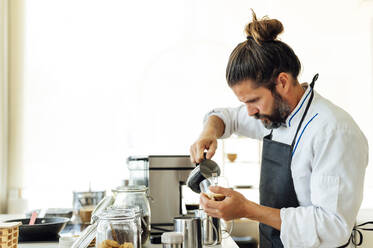 Professioneller Koch gießt Milch ein, während er Kaffee in einem modernen Restaurant zubereitet - PGF00602