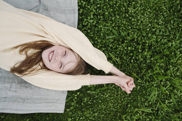 Happy girl lying on mat in grass at public park - EYAF01629