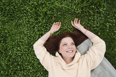 Happy mature woman lying on grass at public park - EYAF01631