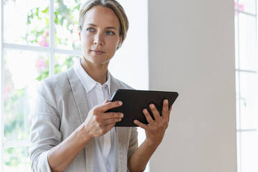 Geschäftsfrau mit digitalem Tablet, die im Büro wegschaut - SBOF03917