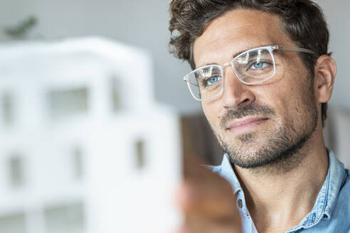 Geschäftsmann mit Brille betrachtet ein Hausmodell - SBOF03954
