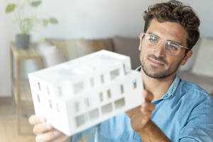 Männlicher Unternehmer mit Brille hält Architekturmodell im Büro - SBOF03955