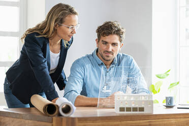 Ein Architekt und eine Architektin arbeiten gemeinsam an einem futuristischen digitalen Tablet im Büro - SBOF03961