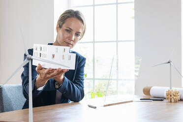 Businesswoman checking architectural model by futuristic device screen at office - SBOF03986