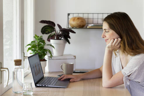 Weibliche Fachkraft mit Hand am Kinn arbeitet am Laptop im Büro zu Hause - AFVF08805