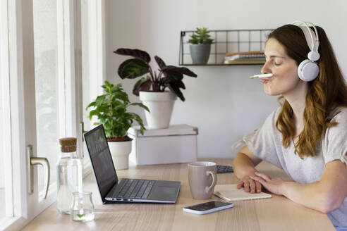 Sorglose Geschäftsfrau, die während eines Videogesprächs im Büro zu Hause einen Stift auf dem Mund balanciert - AFVF08809