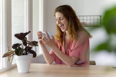 Cheerful woman using smart phone on table at home - AFVF08823