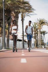 Lächelndes Paar, das auf dem Fußweg einen elektrischen Roller fährt - MPPF01870