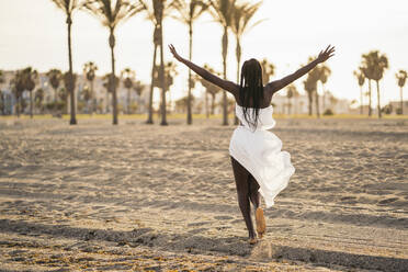 Carefree teenage girl with arms outstretched running on sand - MPPF01881