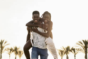 Cheerful man piggybacking girlfriend at beach - MPPF01885