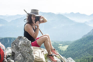 Woman photographing with analog camera while sitting on rock - HHF05658