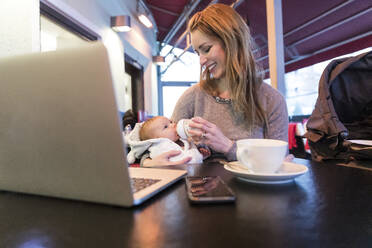 Lächelnde Mutter füttert ihr kleines Mädchen mit Milch, während sie sich von einem Café aus selbstständig macht - WPEF04801