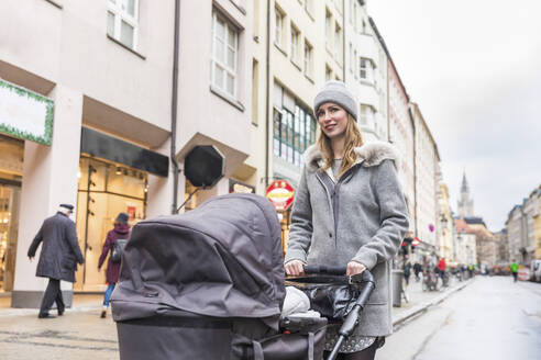 Mutter schiebt Kinderwagen beim Gehen auf der Straße in der Stadt - WPEF04805