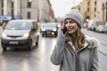 Lächelnde erwachsene Frau, die beim Spazierengehen in der Stadt mit ihrem Handy telefoniert - WPEF04808