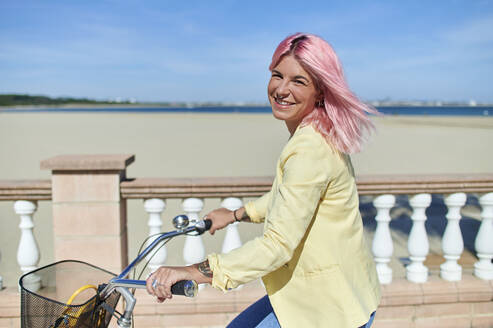 Smiling young woman riding bicycle at beach - KIJF03955