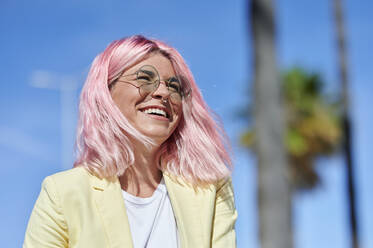 Fröhliche junge Frau mit rosa Haaren, die an einem sonnigen Tag wegschaut - KIJF03963