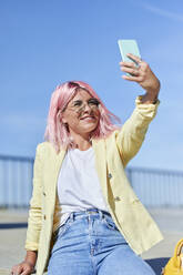 Pinkhaarige Frau nimmt Selfie durch Handy an der Promenade - KIJF03965