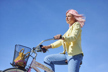 Frau mit rosa Haaren lächelnd beim Fahrradfahren an einem sonnigen Tag - KIJF03974