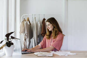 Lächelnde Modedesignerin arbeitet zu Hause am Laptop - AFVF08834