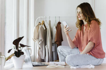 Female entrepreneur using mobile phone while sitting on table at home - AFVF08840