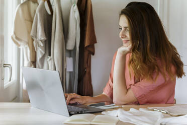 Lächelnde Modedesignerin mit Laptop bei der Arbeit zu Hause - AFVF08843