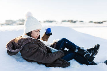 Frau hält Kaffeetasse und entspannt sich im Schnee im Urlaub - MRRF01255